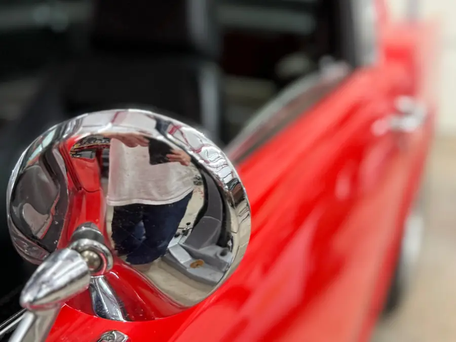 Close-up of a chrome bullet side mirror on a red classic car